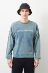 Man wearing indigo blue Ziggy sweatshirt with 'Harder than before' embroidery, paired with a black hat