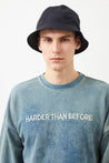 Model showcasing indigo blue Ra Denim sweatshirt and cap, with 'Harder than before' embroidered on the front.